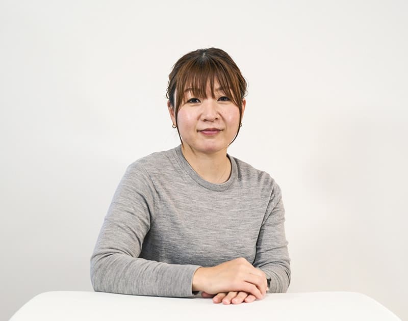福祉用具選定のR.T.さん。グレーのニット姿で机に手を置いている