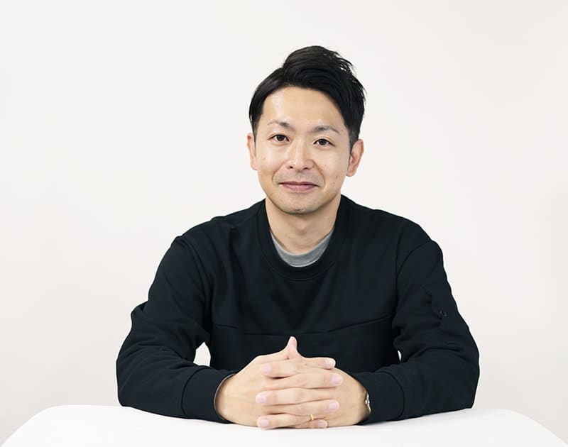福祉用具配送のT.M.さん。黒いトレーナー姿で手を組んでいる