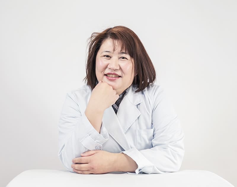 薬剤師のR.Y.さん。白衣姿で頬づえをついている