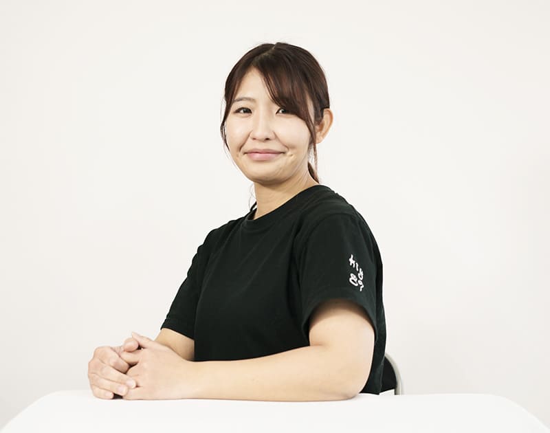 ヘルパーのK.Y.さん。黒いユニフォーム姿で机に手を置いている