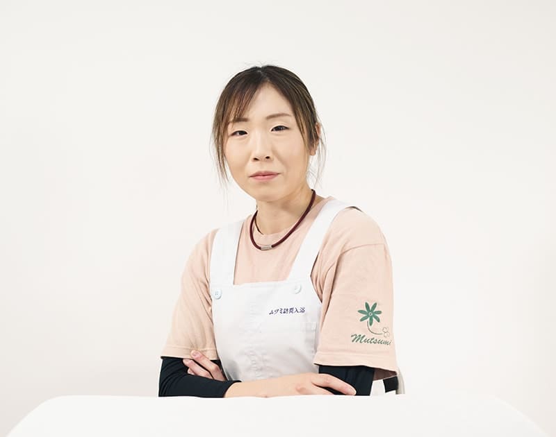 訪問入浴オペスタッフのR.M.さん。白いエプロンを着けて腕を組んでいる