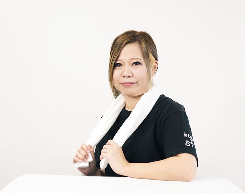 訪問入浴ケアスタッフのS.A.さん。黒いユニフォームに白いタオルを掛けている