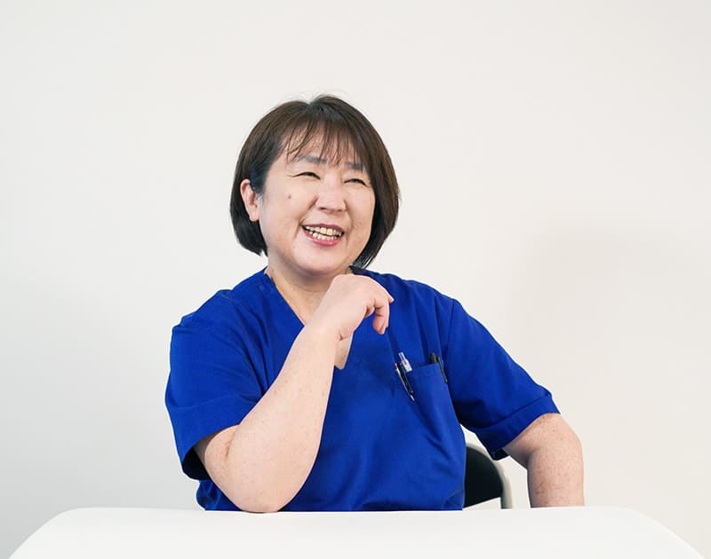 訪問看護師のY.S.さん。青いスクラブ姿で笑っている