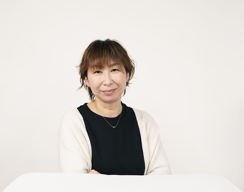 事業所管理者のK.Y.さん。白いカーディガン姿で机に手を置いている